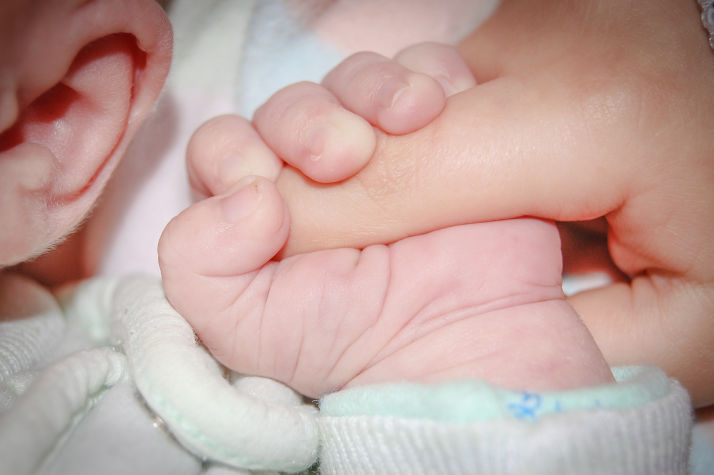 Newborn baby holding mom's finger