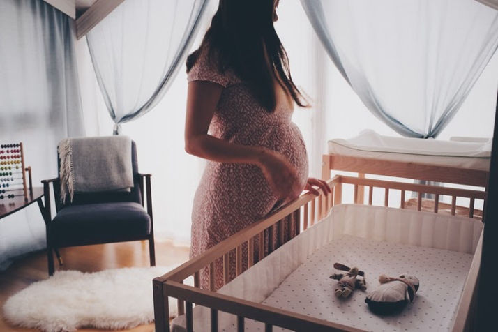 Pregnant woman standing next to crib